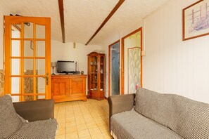 Un salon avec deux canapés à motifs, un meuble en bois, un téléviseur et une porte donnant sur une autre pièce.