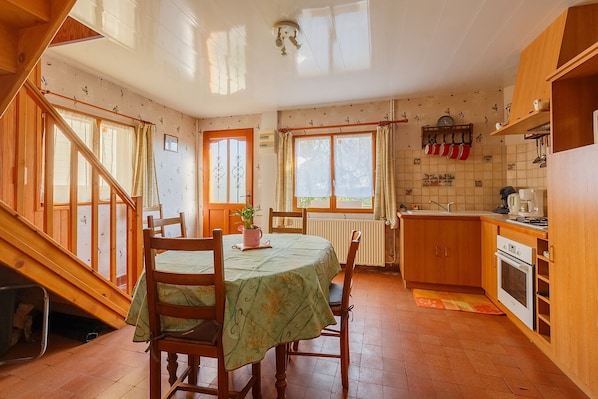 Une cuisine avec des meubles de rangement en bois, une table à manger avec des chaises, un escalier et une fenêtre avec des rideaux.