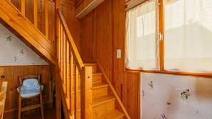 Un escalier en bois menant à un niveau supérieur, une chaise et une fenêtre ornée d’un motif floral.