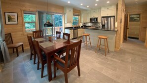 A modern kitchen with wooden cabinets, a stainless steel refrigerator, and a dining area with a wooden table and chairs.