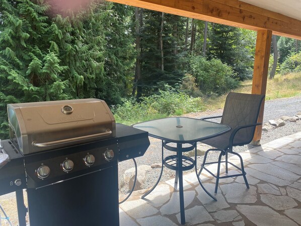 A barbecue grill with four burners, a glass table, and two chairs under a wooden pergola. - NEW Private Forest Lodge 6 Mins from Ferry/Town Sleeps 8 (Eastsound)