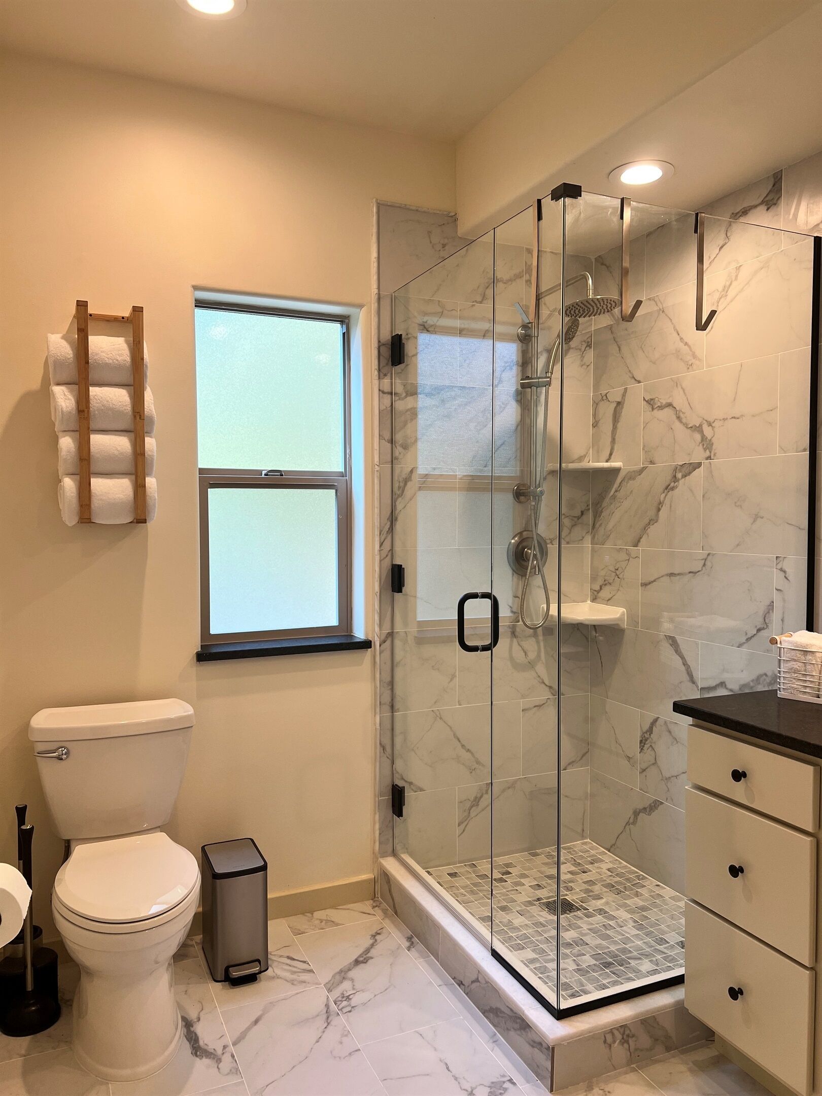 Un bagno moderno con cabina doccia in vetro, piastrelle in marmo, un water e una finestra.