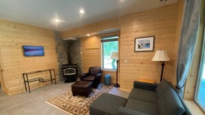 A cozy living room with a stone fireplace, a sofa, a coffee table, and a television on the wall.