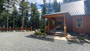 A wooden cabin with a porch, surrounded by a gravel driveway and a wooden fence.