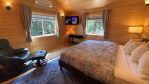 A cozy room with a bed, a chair, a desk, and a TV on the wall.