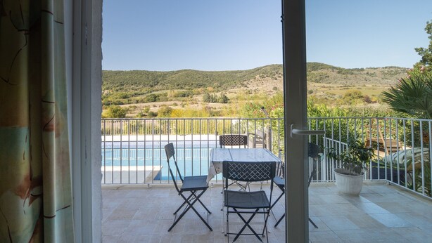 A balcony with a pool, outdoor seating, and a view of a hilly landscape.