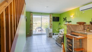 A room with a wooden staircase, a sliding glass door leading to an outdoor area, a kitchen with a sink and a TV, and a sofa.