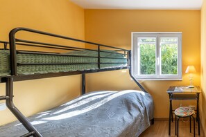 A bunk bed room with a window, a small table with a lamp, and a chair.