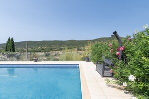 A swimming pool with a view of hills, a metal fence, and some greenery.