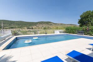 Ein Swimmingpool mit Blick auf Hügel, umgeben von einem weißen Zaun und blauen Liegestühlen.