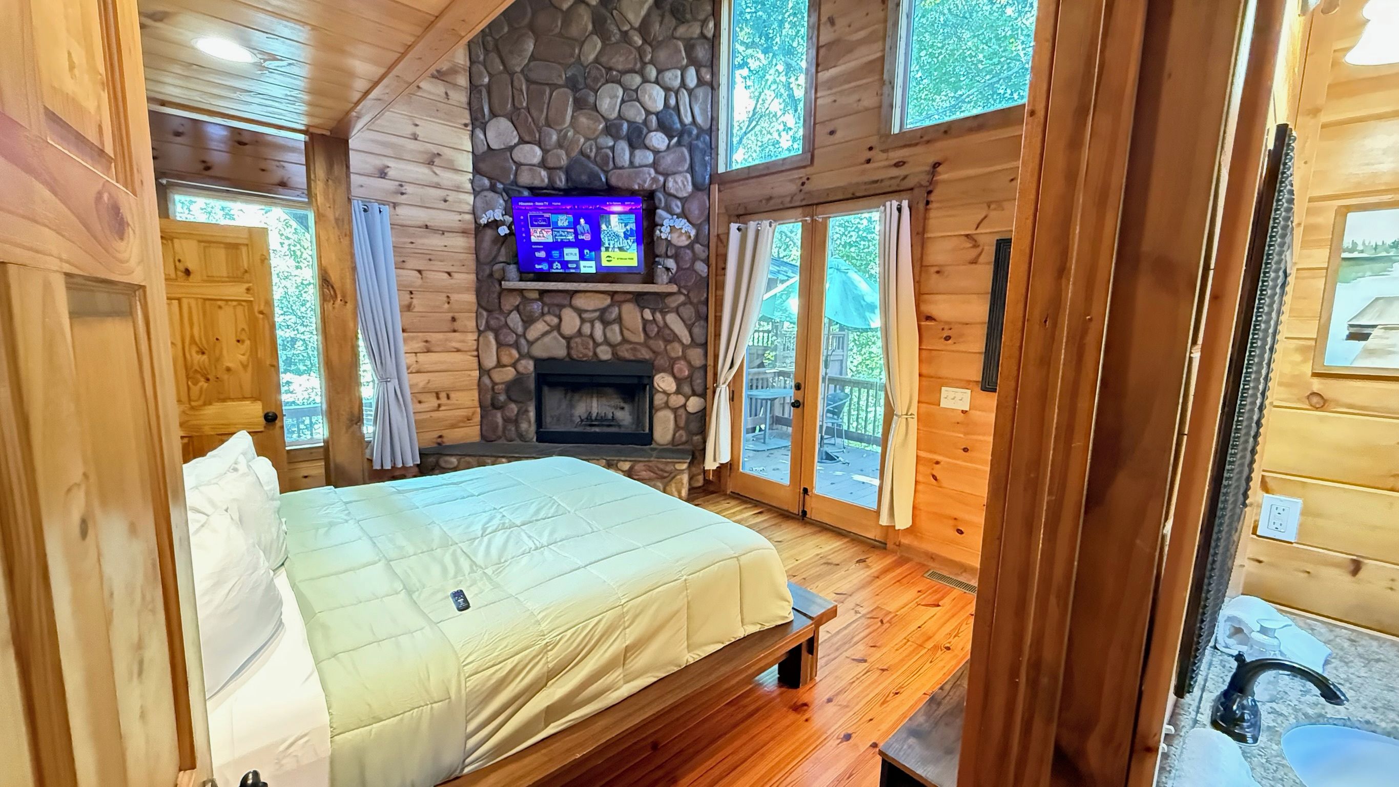 A wooden cabin bedroom with a stone fireplace, a bed, and a television mounted on the wall.