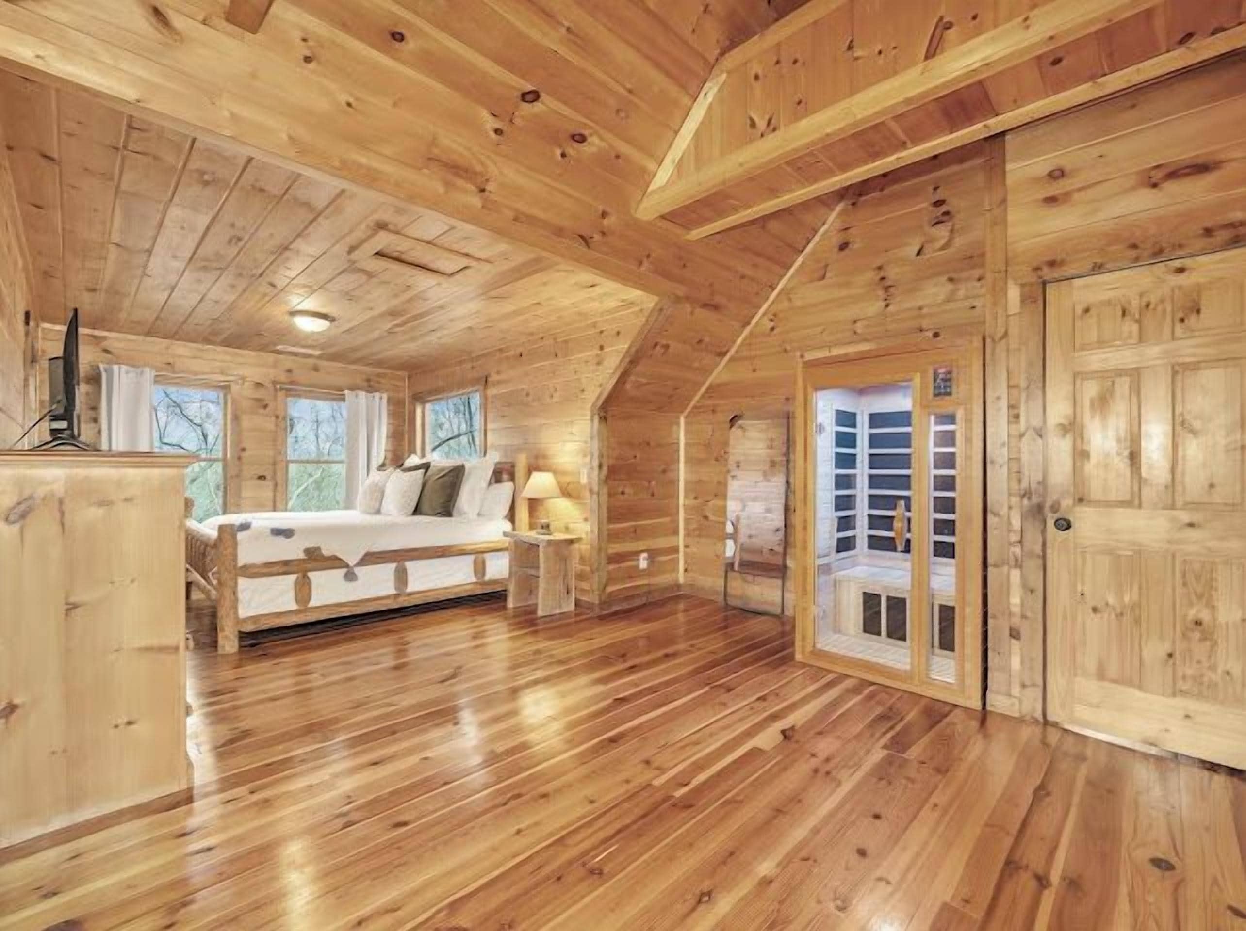 Ein Interieur einer Holzhütte zeigt ein Schlafzimmer mit einem Bett, einem Nachttisch und einem Fenster.