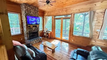 A wooden cabin interior with a stone fireplace, leather sofas, and large windows.
