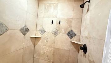 A shower area with beige tiles and a few gray diamond-shaped tiles. There are two black fixtures, one on the wall and one on the floor.