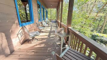 A wooden deck with outdoor seating and a view of a forest.