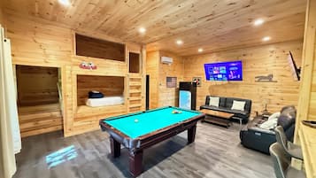 Een houten interieur met een pooltafel, een bank en een televisie.