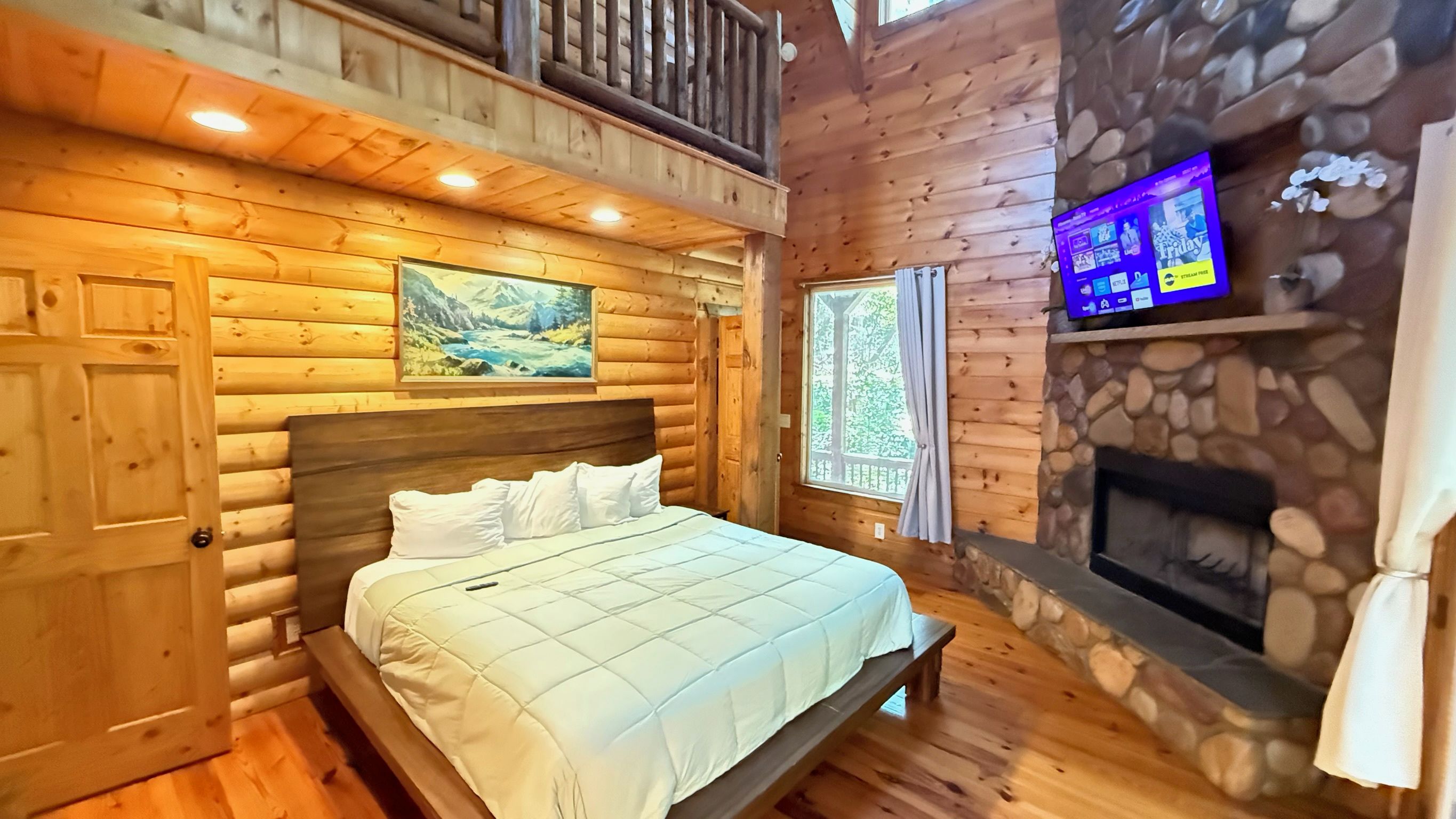 Quarto de cabana de toras com cama, lareira de pedra e televisão fixada na parede.