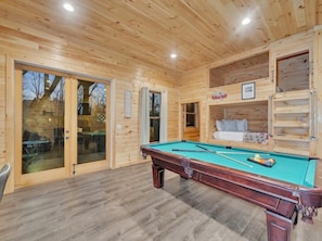 A pool table in a wooden room with a sliding glass door leading outside.