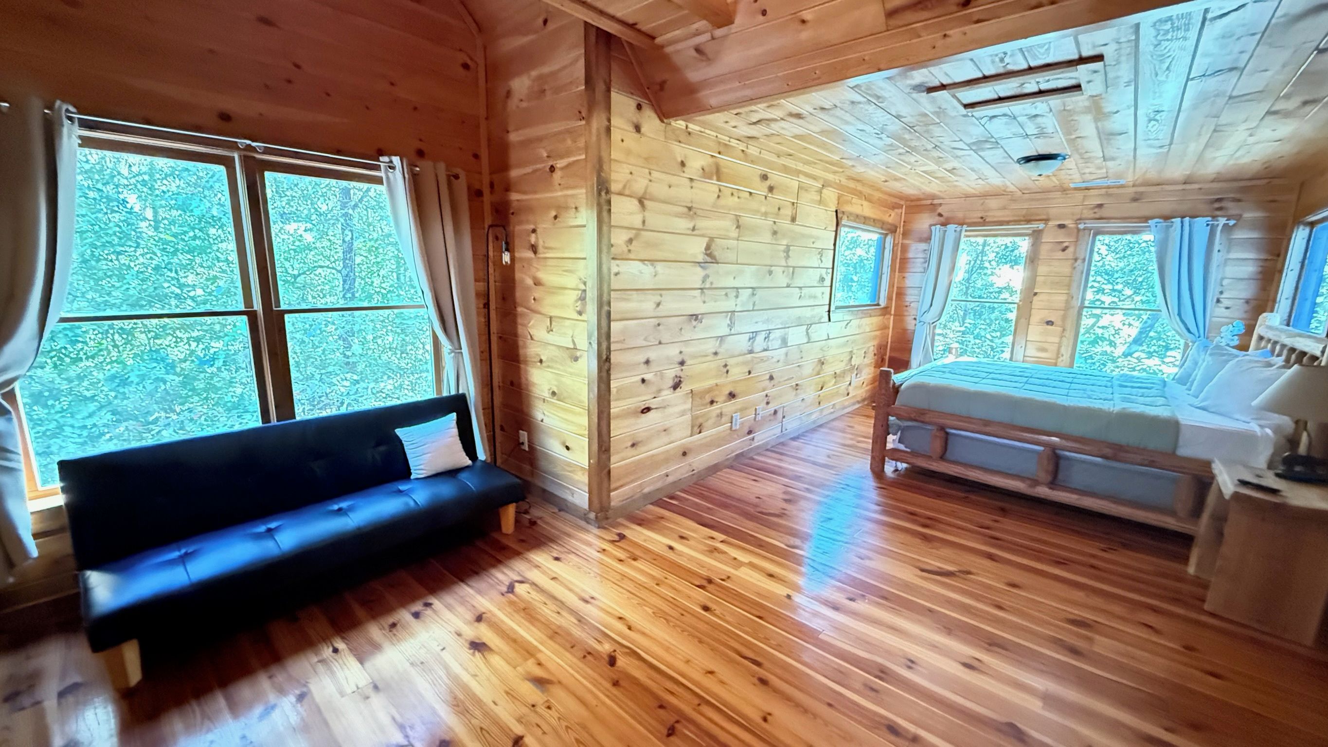 Interno di una baita in legno con un divano, un letto e ampie finestre.