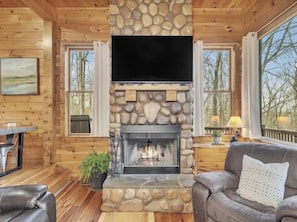 A cabin interior with a stone fireplace, wooden walls, a leather sofa, and a television.