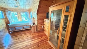 A wooden cabin bedroom with a bed, dresser, and a window with curtains.