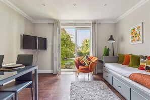A modern room with a flat-screen TV, a dining table with chairs, a sofa with colorful cushions, and a large window with a view of greenery. - Ground Floor•Parking•Windsor Castle - By Tempstay (Berkshire)