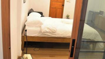 A bedroom with a wooden door, a bed with white bedding, and a small bedside table.
