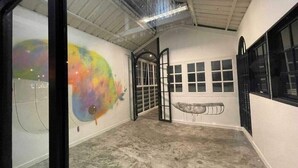 Un espacio interior con piso de concreto, un gran mural abstracto en la pared izquierda y una puerta que conduce a otra habitación.