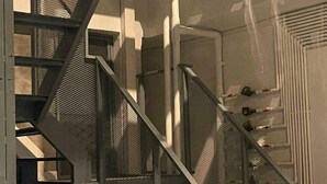 Una escalera de metal con barandilla de malla, que lleva a una puerta con marco blanco.