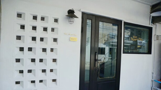 Fachada de edificio con una puerta negra, una luz empotrada en la pared y una ventana con el rótulo 'BAAN PROMPT PACK'.