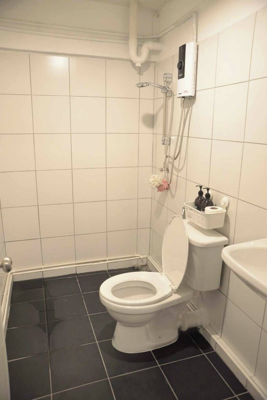 A small, modern bathroom with a white toilet, a shower unit, and a black-tiled floor.
