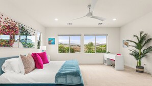 Un dormitorio con cama, escritorio, silla y un amplio ventanal con vistas a zonas verdes.