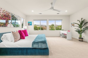 A bedroom with a bed, a desk, a chair, and a large window with a view of greenery. - Resort-Style Escape with Pool, Spa, BBQ & Fire Pit (La Quinta)