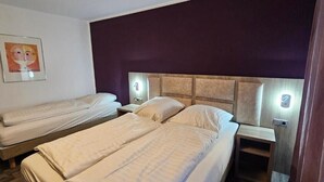 A hotel room with two single beds, a nightstand with a lamp, and a wall-mounted artwork.