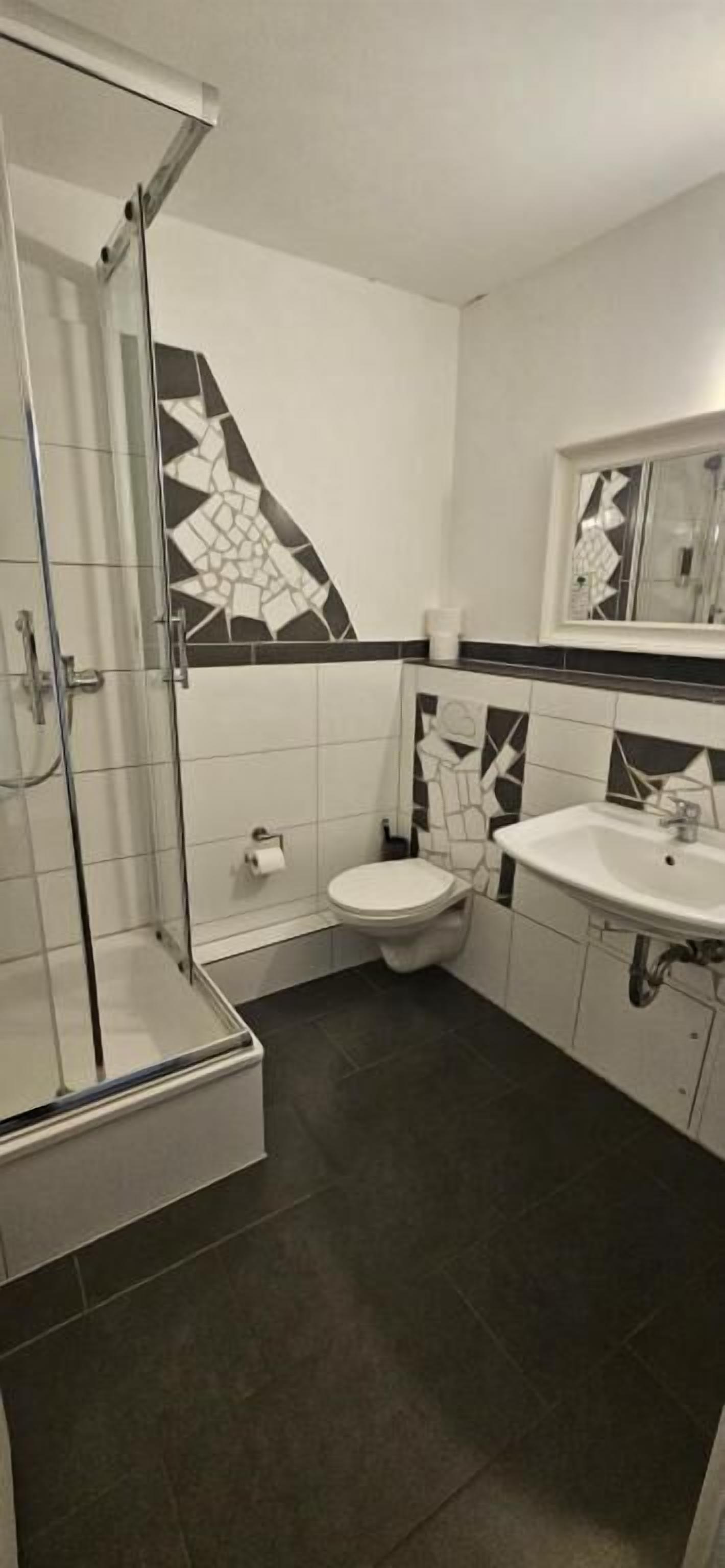A bathroom with a shower, toilet, sink, and patterned tiles.