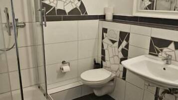 A bathroom with a shower, toilet, sink, and patterned tiles.