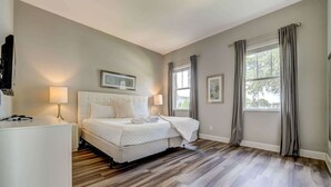 A bedroom with a bed, two bedside lamps, a flat-screen TV, and a large window with curtains. - 5BR family retreat w/ pool & game room (Kissimmee)