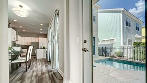 A modern kitchen with white cabinets, a dining area with a table and chairs, and a view of a swimming pool outside. - 5BR family retreat w/ pool & game room (Kissimmee)