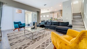 A modern living room with a sofa, a yellow armchair, and a glass coffee table. - 5BR family retreat w/ pool & game room (Kissimmee)