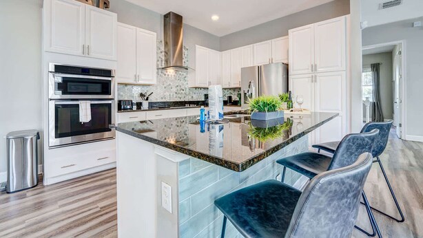 A modern kitchen with white cabinetry, stainless steel appliances, and a central island with seating. - 5BR family retreat w/ pool & game room (Kissimmee)