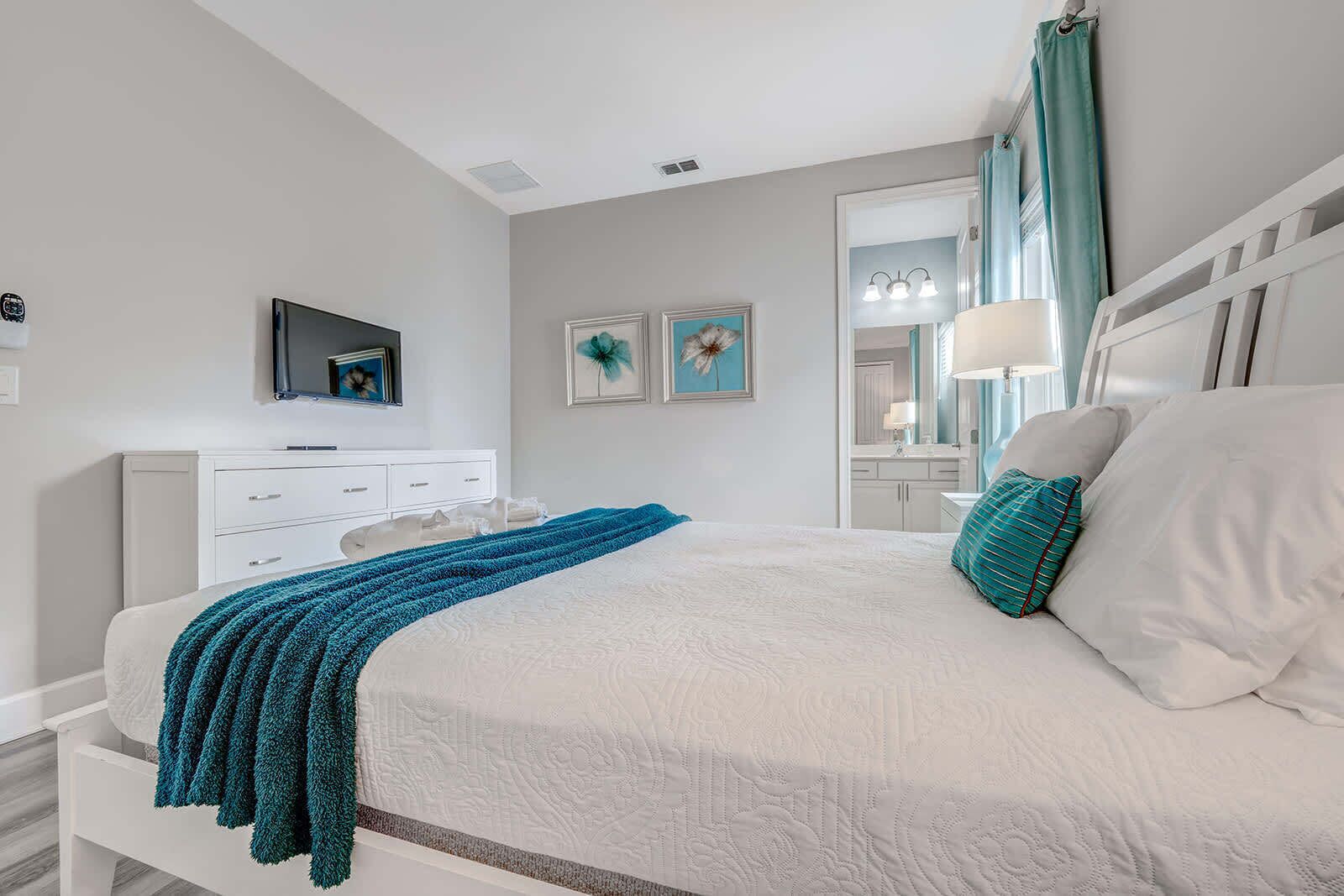 Een slaapkamer met een bed, een dressoir, een televisie en kunst aan de muur.