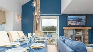 A dining area with a table set for four, a blue sofa, a fireplace, and a scenic view through a glass door.