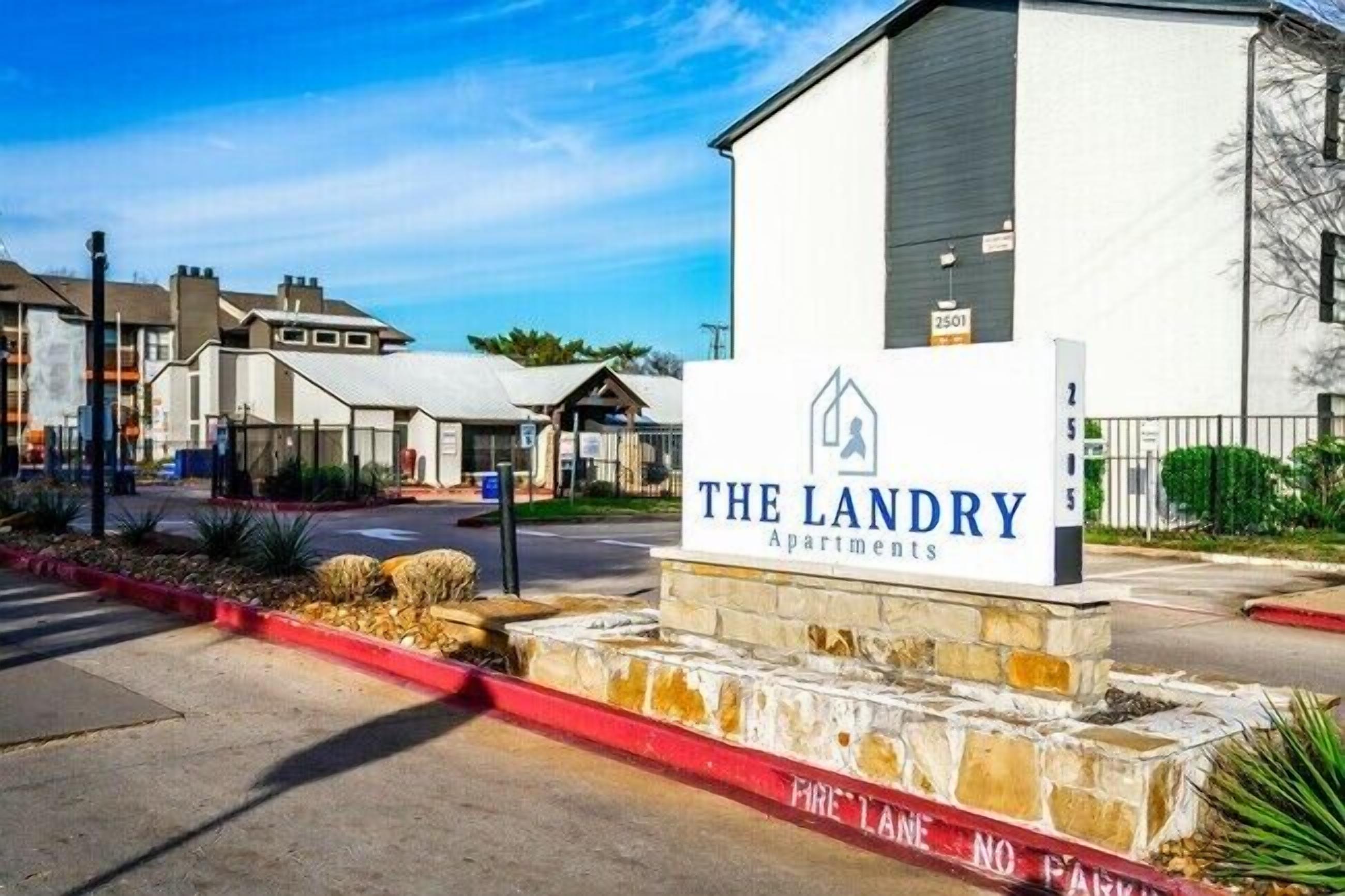 Une enseigne indiquant l’emplacement des appartements « The Landry », avec une vue dégagée sur l’entrée et les bâtiments environnants.