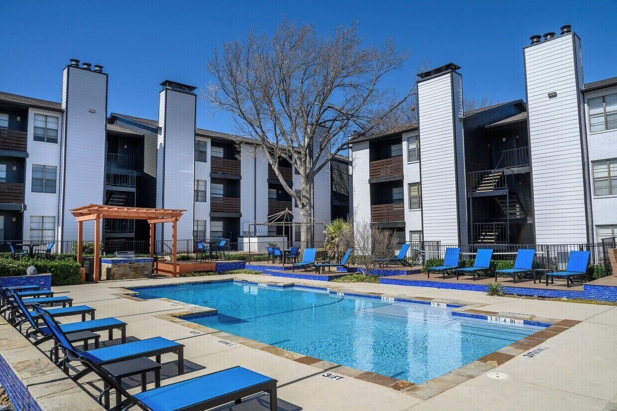 A swimming pool with lounge chairs and a gazebo, surrounded by apartment buildings.