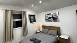 Un dormitorio moderno con una cama grande, una mesita de noche, dos cuadros enmarcados en la pared y una ventana con cortinas.