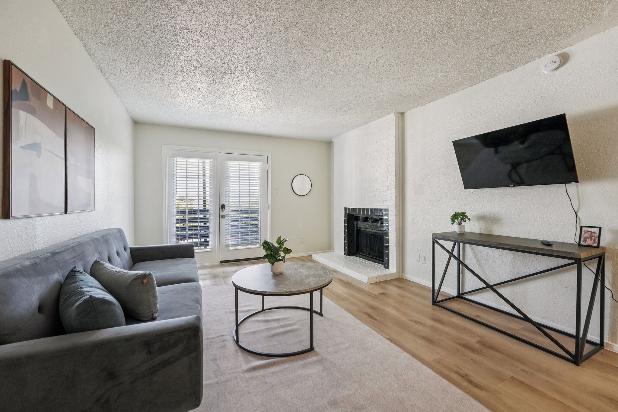 A living room with a grey sofa, a round coffee table, a fireplace, and a TV mounted on the wall.