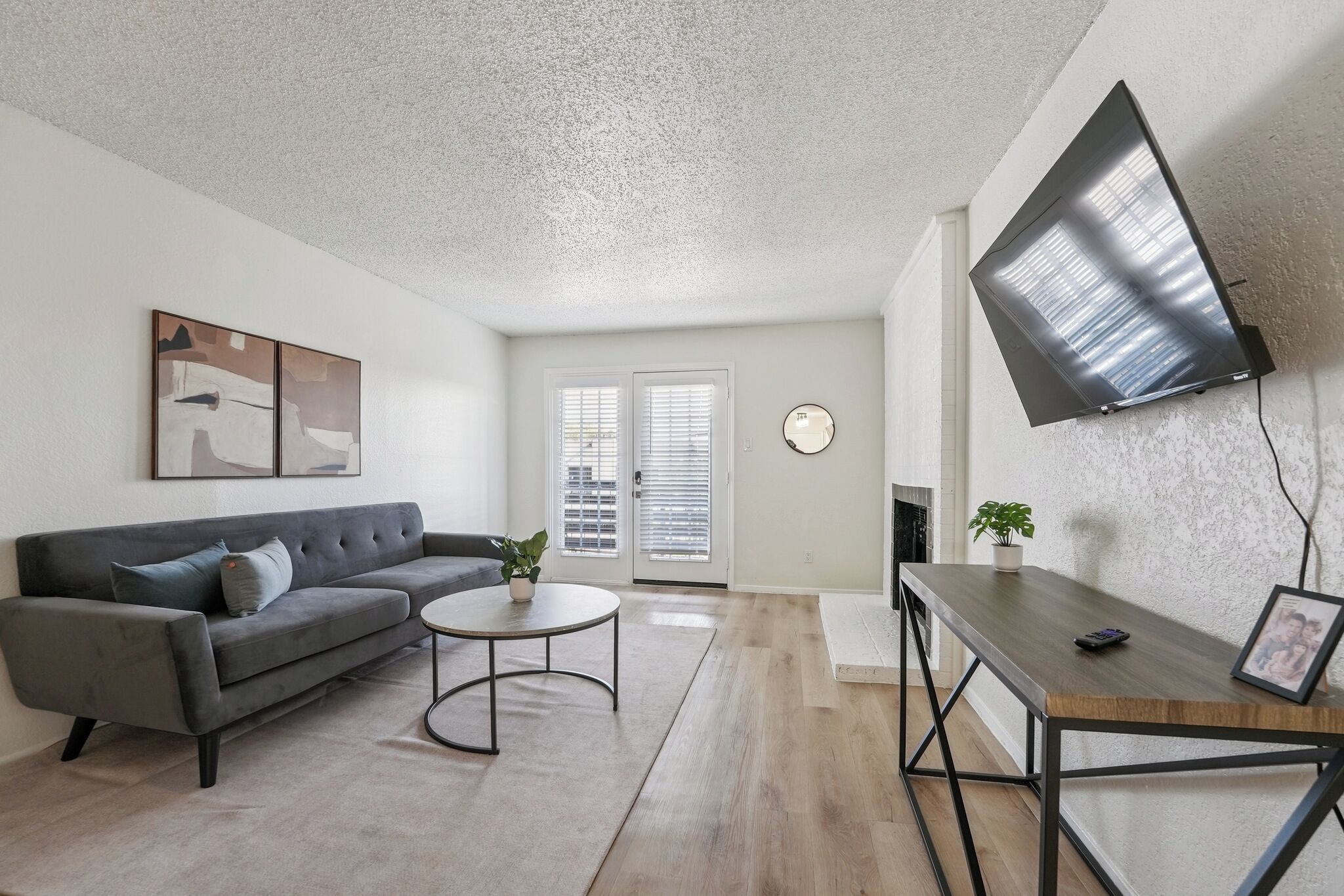 A modern living room with a grey sofa, a round coffee table, a TV mounted on the wall, and a fireplace.