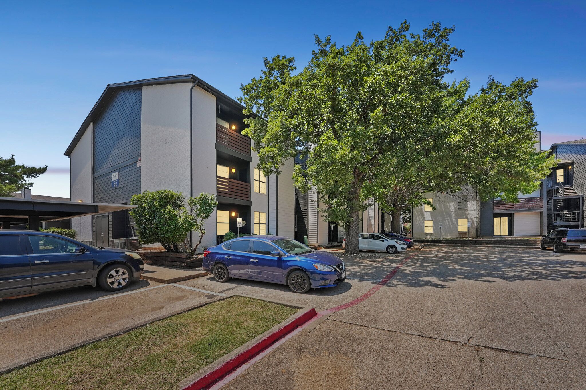 Un bâtiment moderne doté d’un parking, d’arbres et de voitures garées.