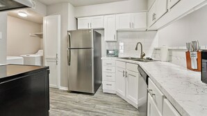 Una cocina moderna con armarios blancos, un refrigerador de acero inoxidable, un microondas y un lavamanos.