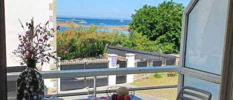 Uma varanda com uma mesa posta para dois, um vaso com flores e vista para o mar.